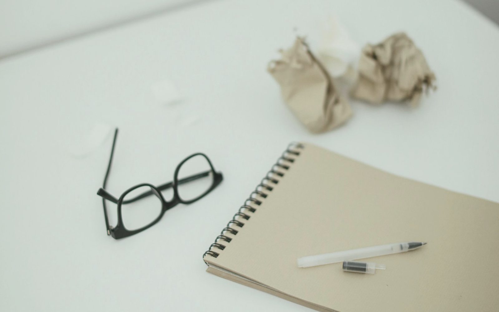 Reading glasses, a notebook and a pen on a plain desk.